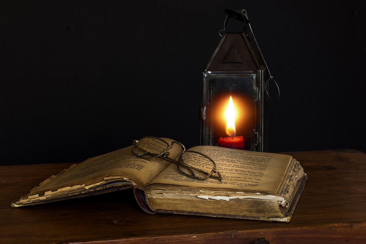 Stara otwarta księga z okularami i paląca się obok świeczka